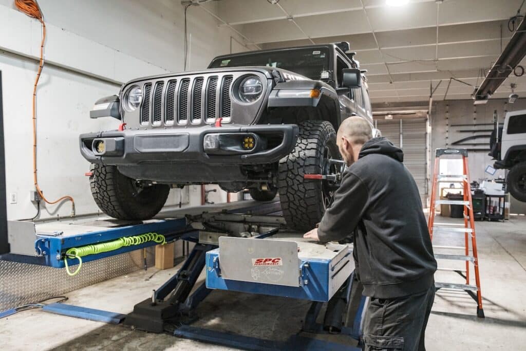Mechanic performing alignment on a lifted Jeep Wrangler JL